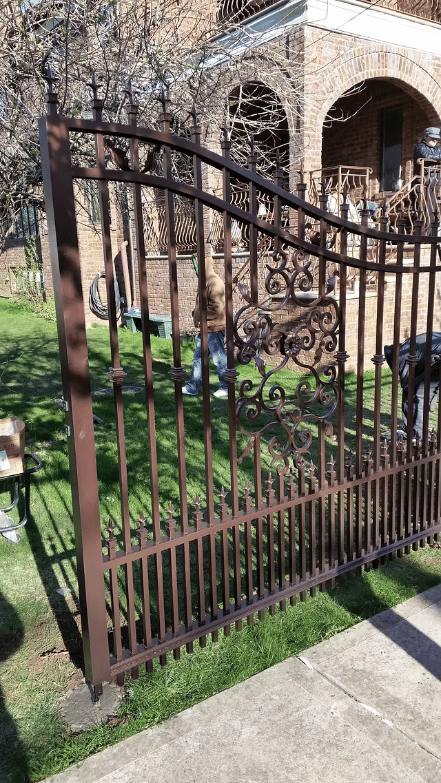 Wrought iron gate with ornate design in a green lawn setting outside a brick building.