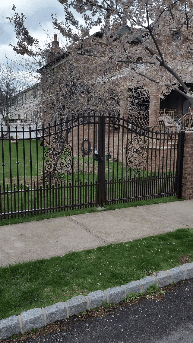 Decorative wrought iron gate with intricate design in a residential property landscape.