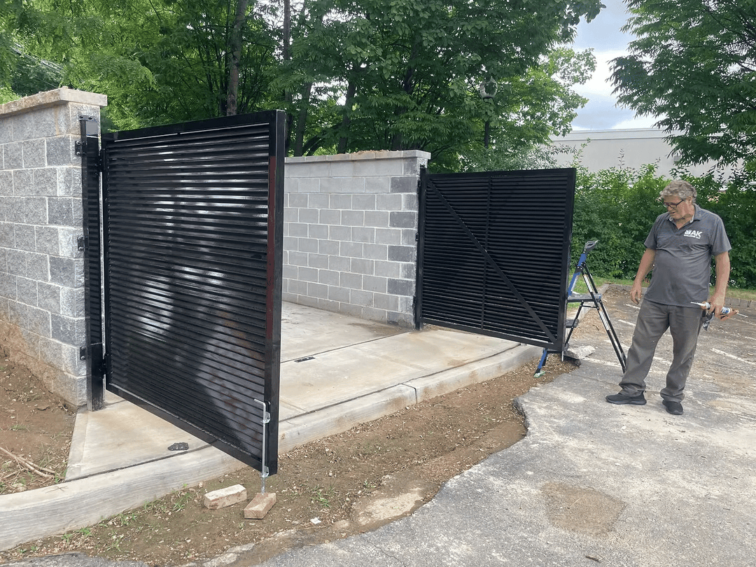 Black sliding gate installation next to a stone wall with a technician inspecting it.