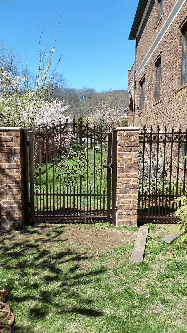 Elegant wrought iron garden gate with brick pillars leading to a lush green garden.