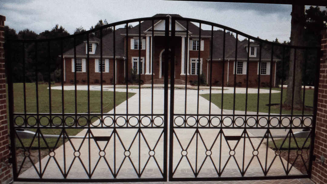 Elegant iron gate opening to a luxury brick mansion with a landscaped driveway.