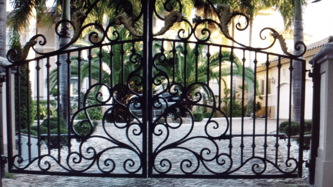 ornate black wrought iron gate with intricate designs and lush tropical landscaping behind it