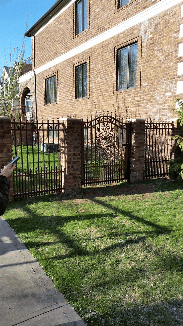 Brick building exterior with a decorative wrought iron fence and green lawn.