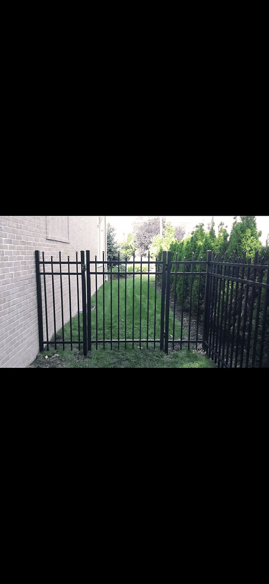 Black metal fence with gate leading to a grassy area beside a brick building.