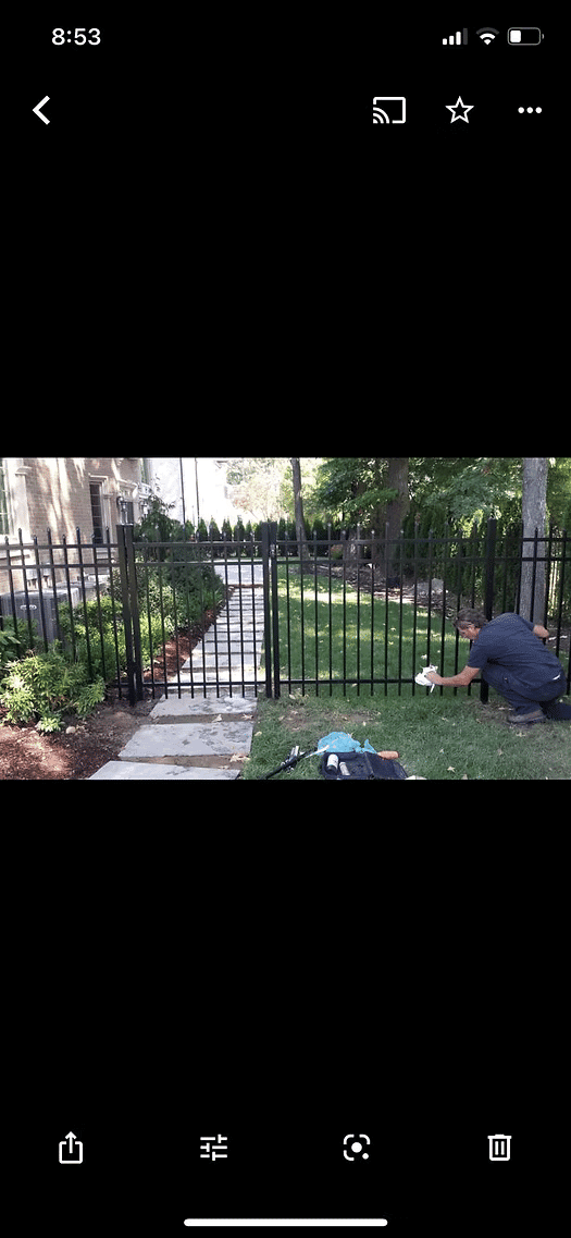 Worker installing a black metal fence in a landscaped yard with stone pathway.