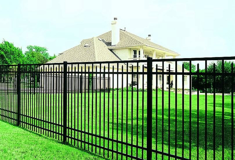 Elegant black metal fence surrounding a spacious green lawn and a large house in the background.