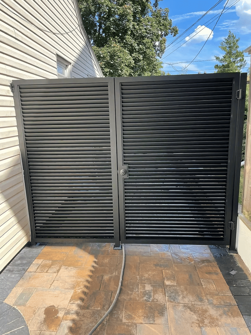 Modern black metal security gate with slats, installed beside a house on a sunny day.