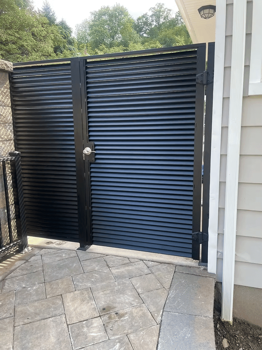 Modern black slatted metal gate with secure lock, set in a stone pathway entrance.
