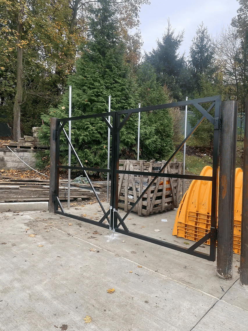 Metal gate installation at a construction site with wood pallets and outdoor scenery.