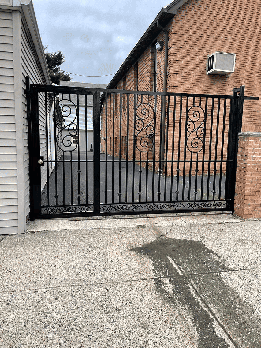 Elegant black wrought iron gate with decorative scrollwork, leading to a brick building.