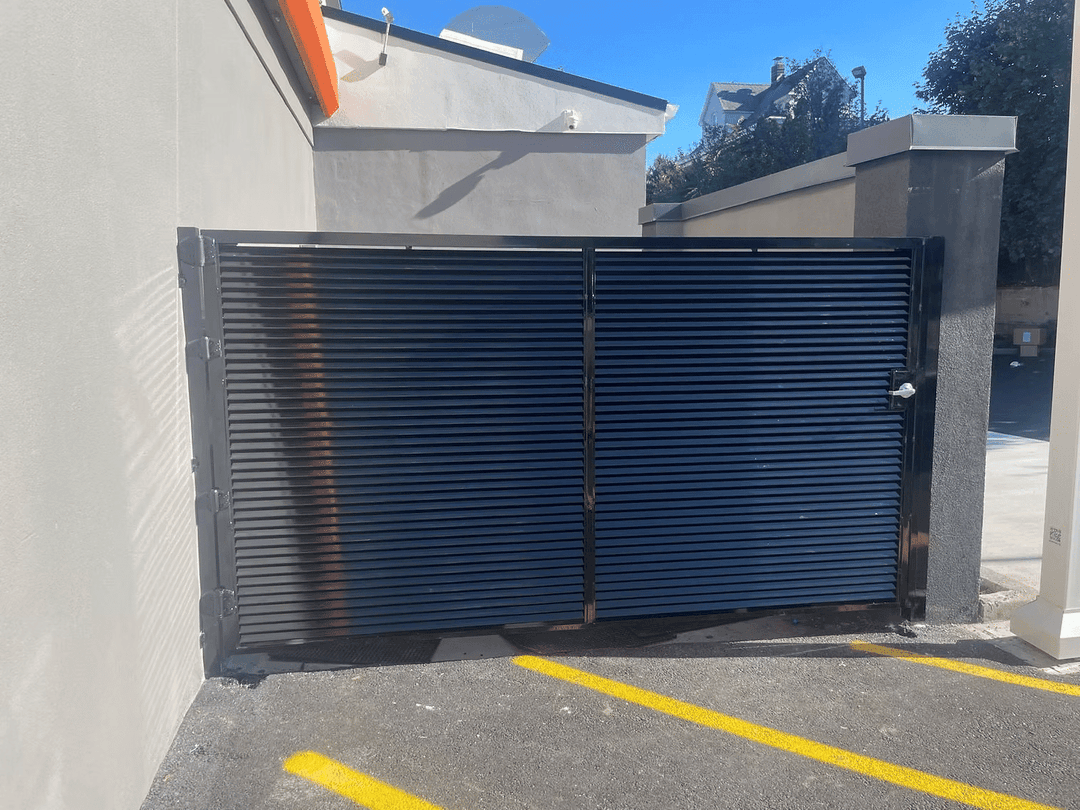 Black horizontal slatted gate at a commercial entrance with yellow parking lines.