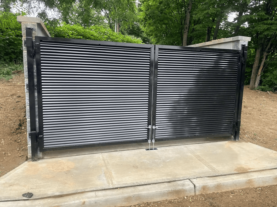 Modern black horizontal slat gate with concrete base, surrounded by greenery.