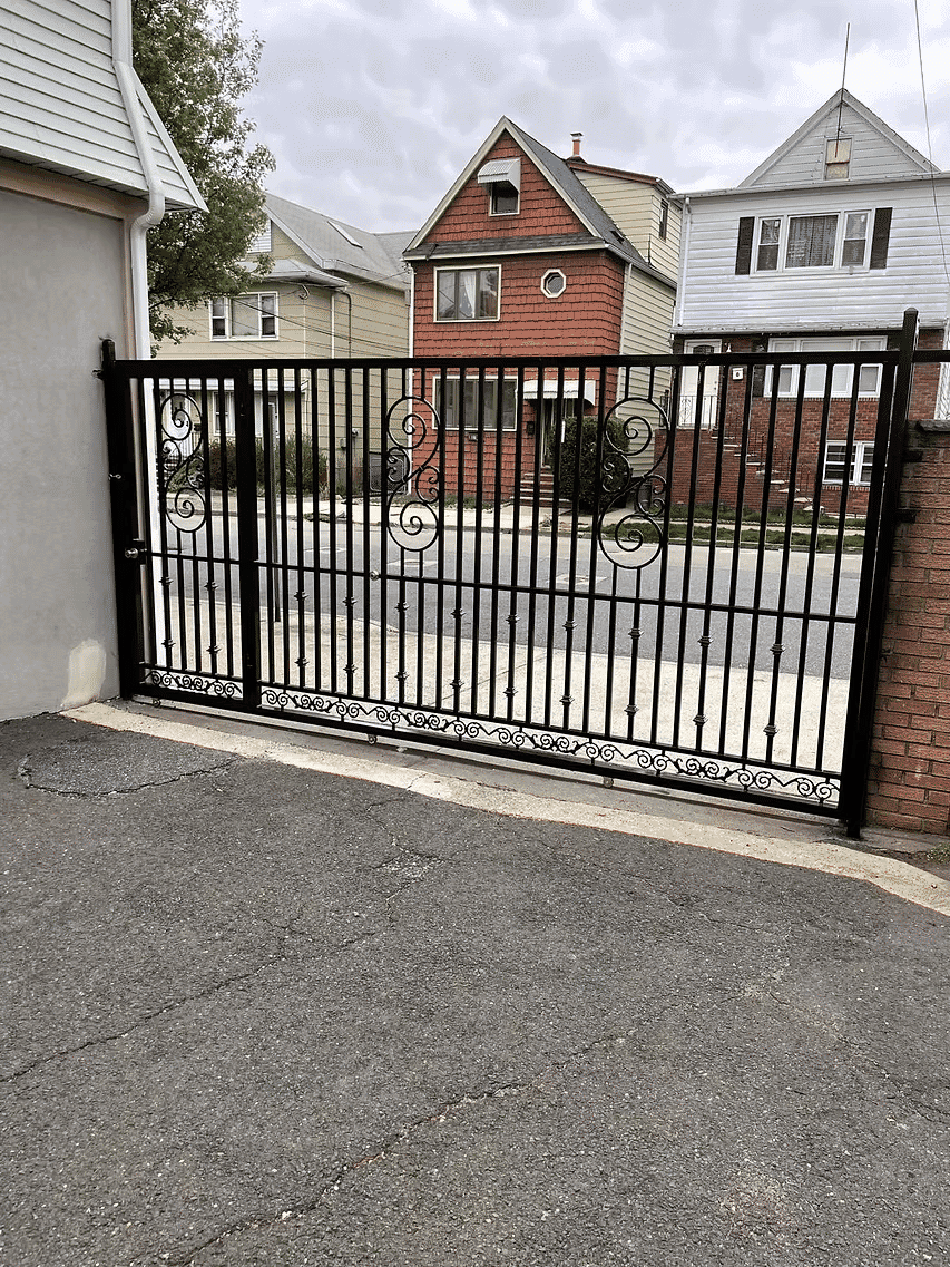 Black metal driveway gate with ornate designs, suburban homes in the background.