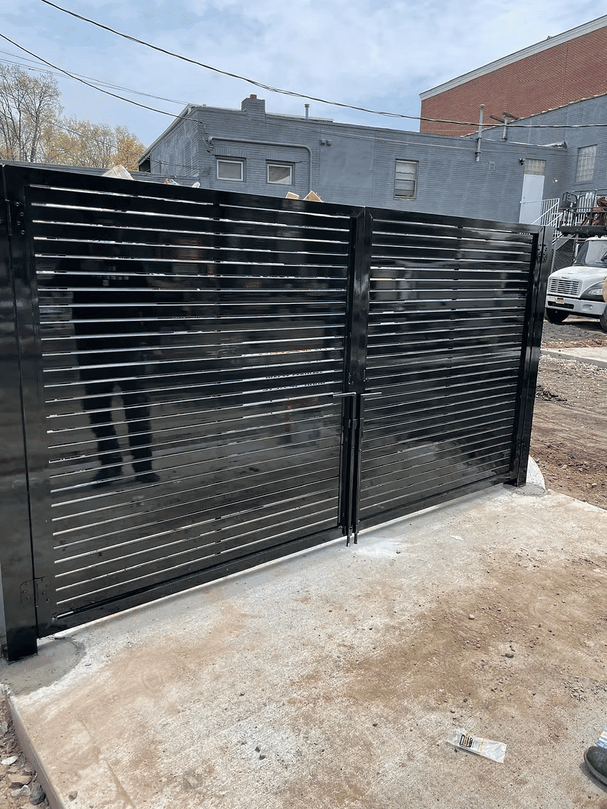 Black slatted gate installed on a concrete base, set against a building backdrop.