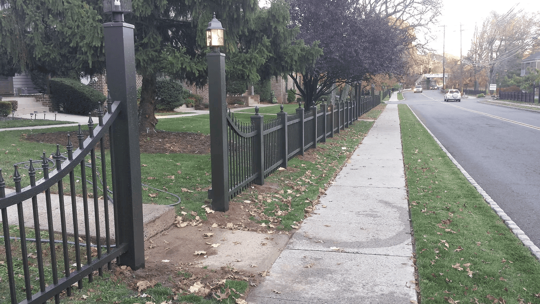 Decorative black fence with lamp posts lining a sidewalk in a suburban neighborhood.