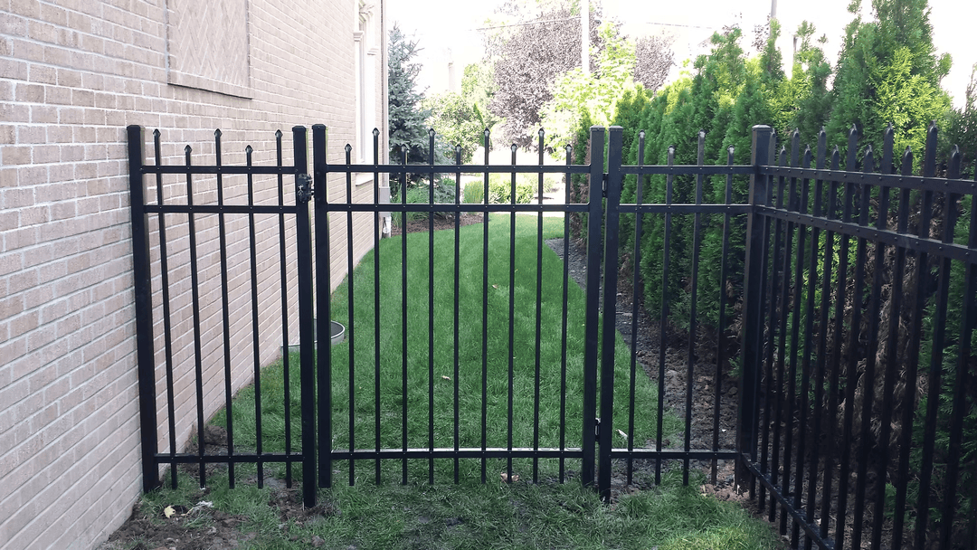 Black iron gate opening to a well-maintained grassy area surrounded by greenery.