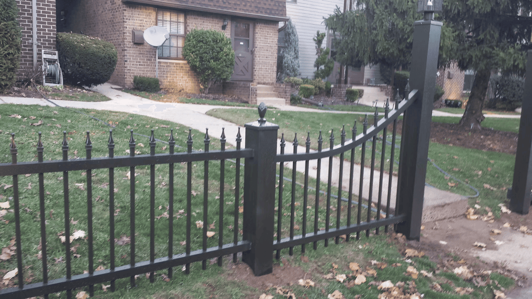 Black decorative metal fence with a curved gate in a residential front yard.