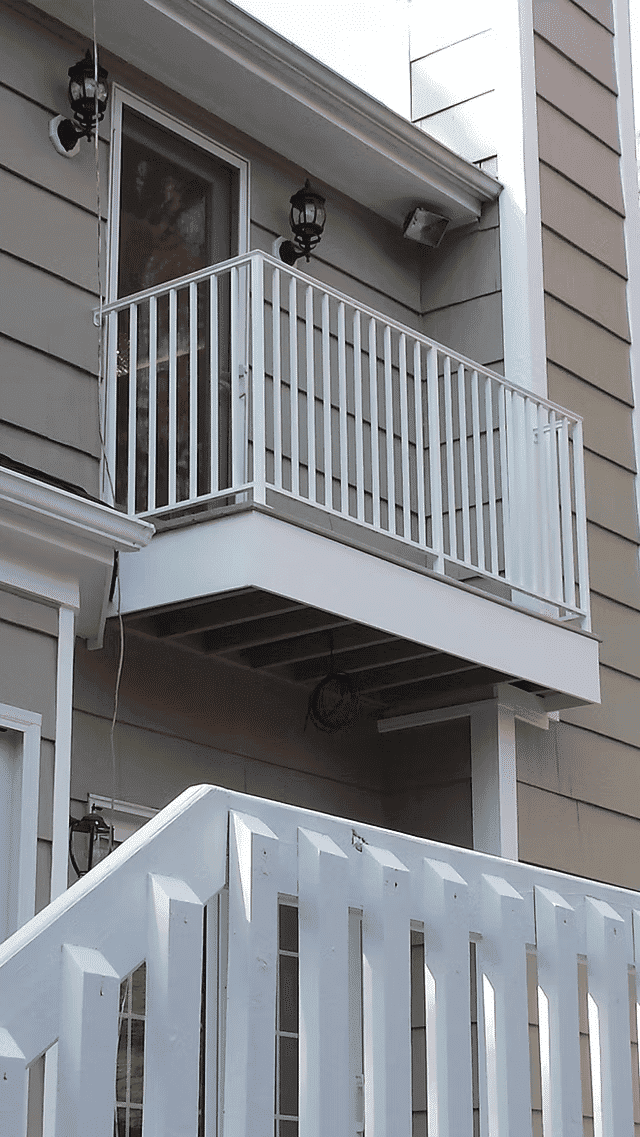 White balcony with railing on a beige house exterior, featuring two lantern lights.