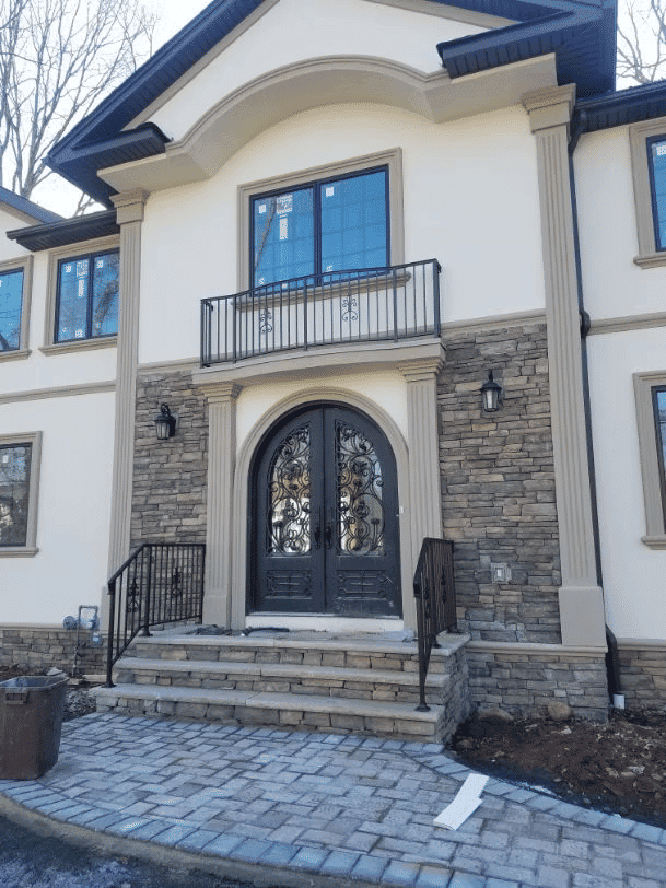 Elegant modern home entrance with stone facade, double doors, and decorative balcony.