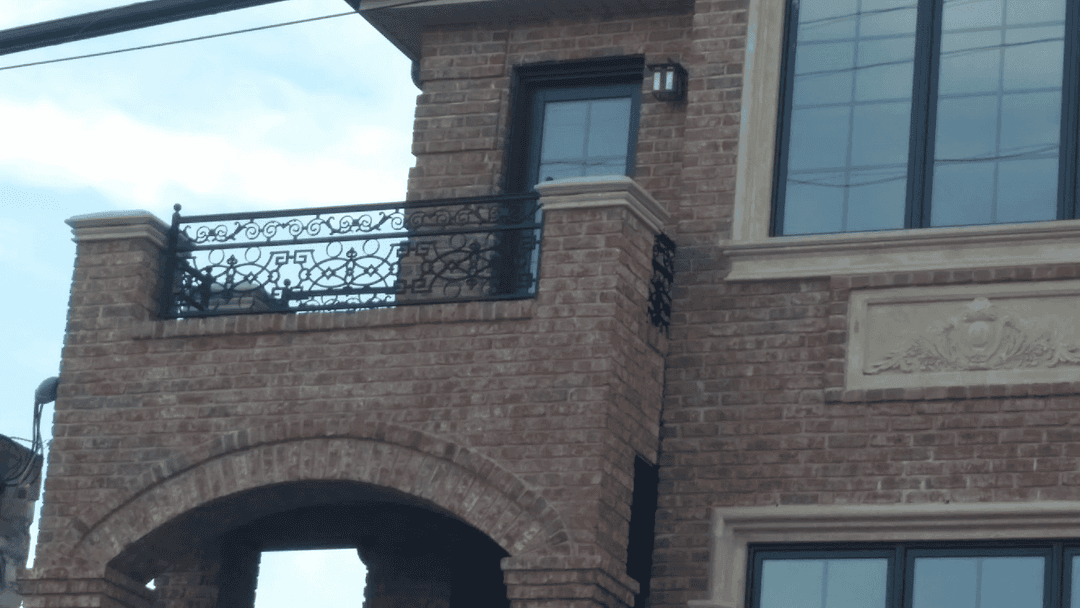 Brick exterior of a building with decorative balcony railing and large windows.
