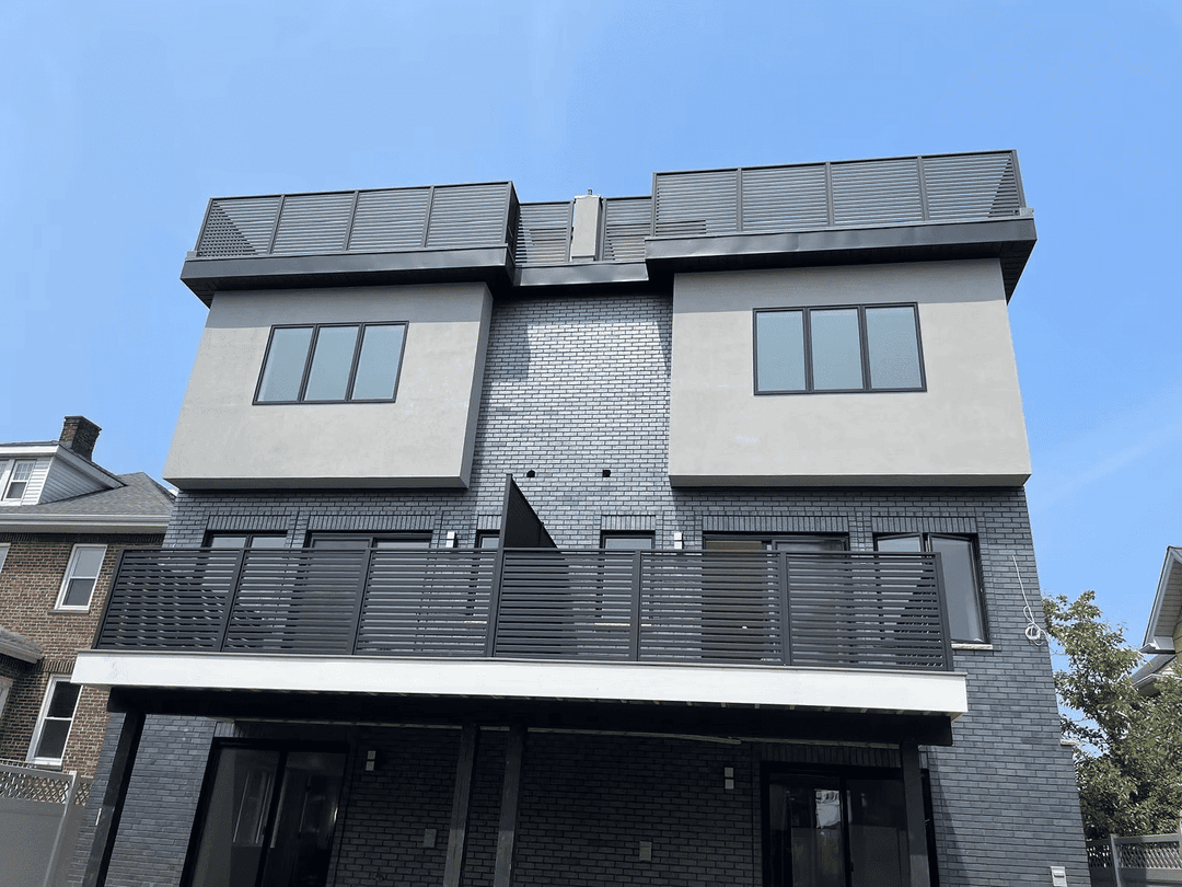 Modern two-story home with a balcony and large windows under a clear blue sky.