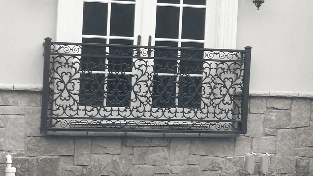 Wrought iron balcony railing with intricate floral design against a stone wall.