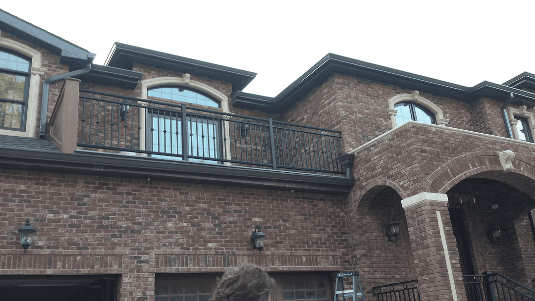 Red brick house with an upper balcony and decorative windows against a clear sky.
