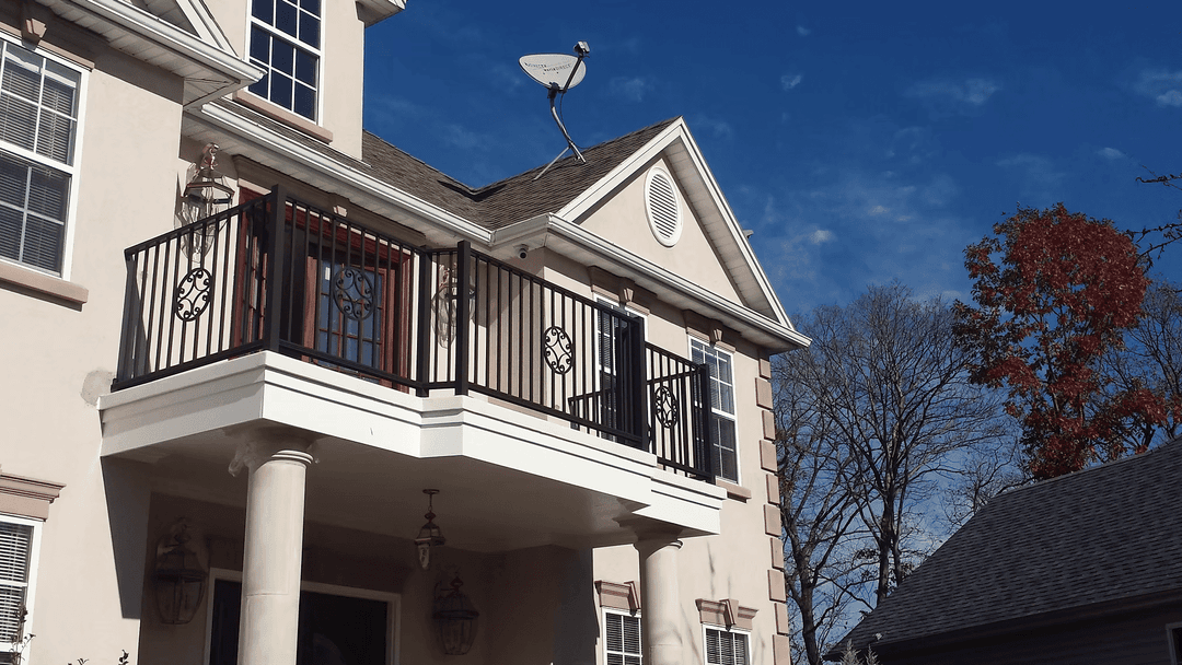 Elegant two-story home with a balcony, satellite dish, and clear blue sky backdrop.