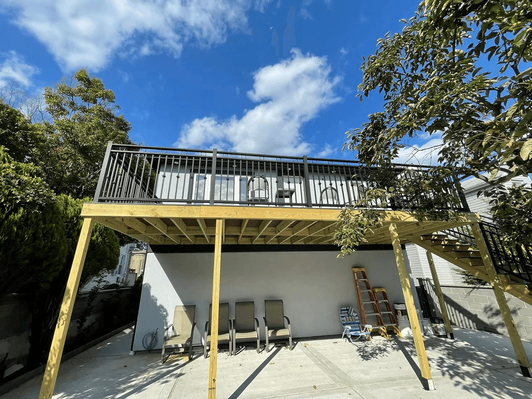 Wooden deck with railing above patio furniture under a blue sky with scattered clouds.