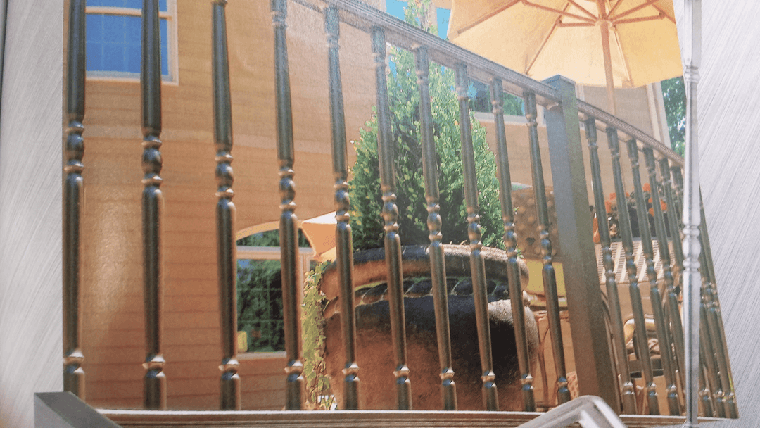 Elegant railing design with round balusters and a sunny patio featuring an umbrella and greenery.
