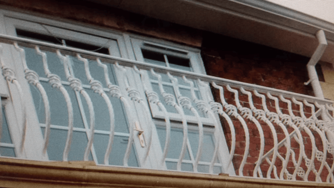 White wrought iron balcony railing on brick building with windows above.
