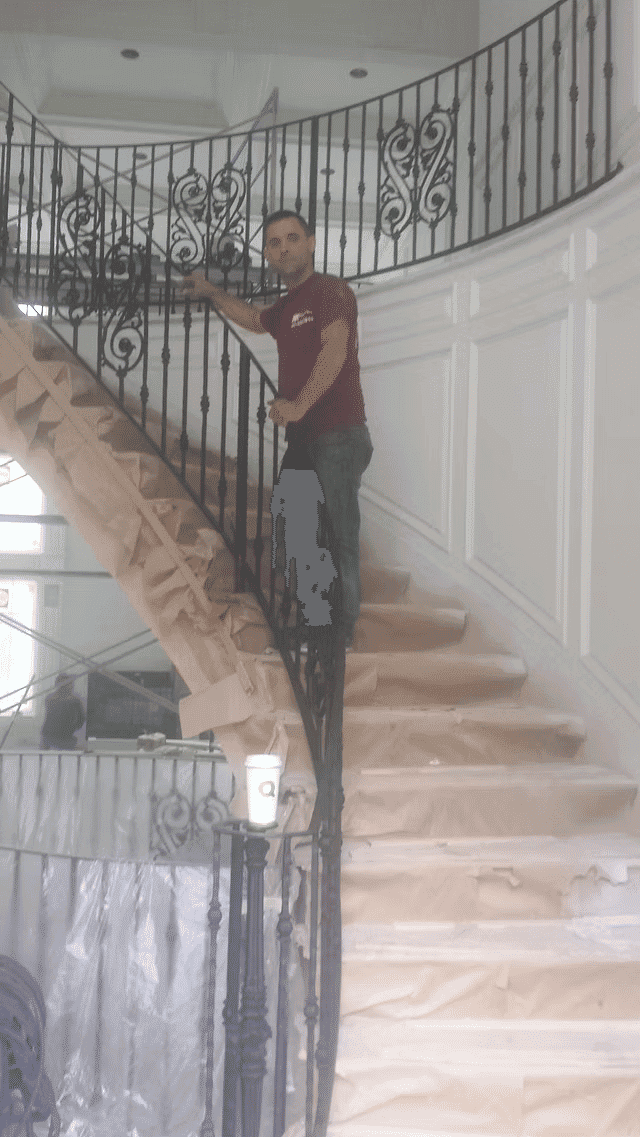 Contractor painting wrought iron staircase in upscale home with protective coverings.