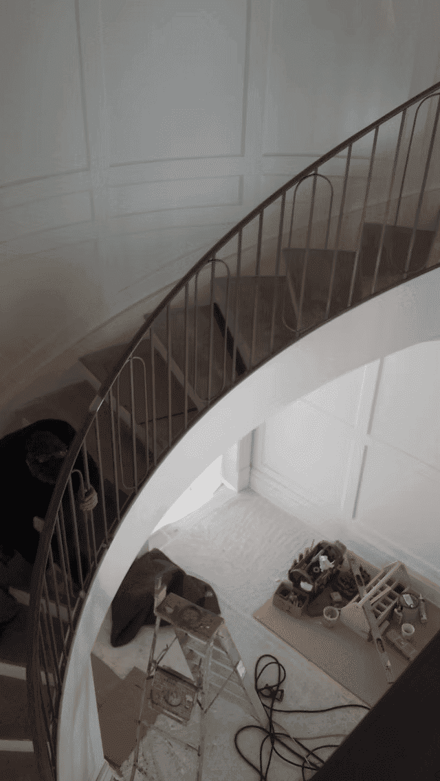 Curved staircase with a worker doing renovations and tools neatly arranged below.
