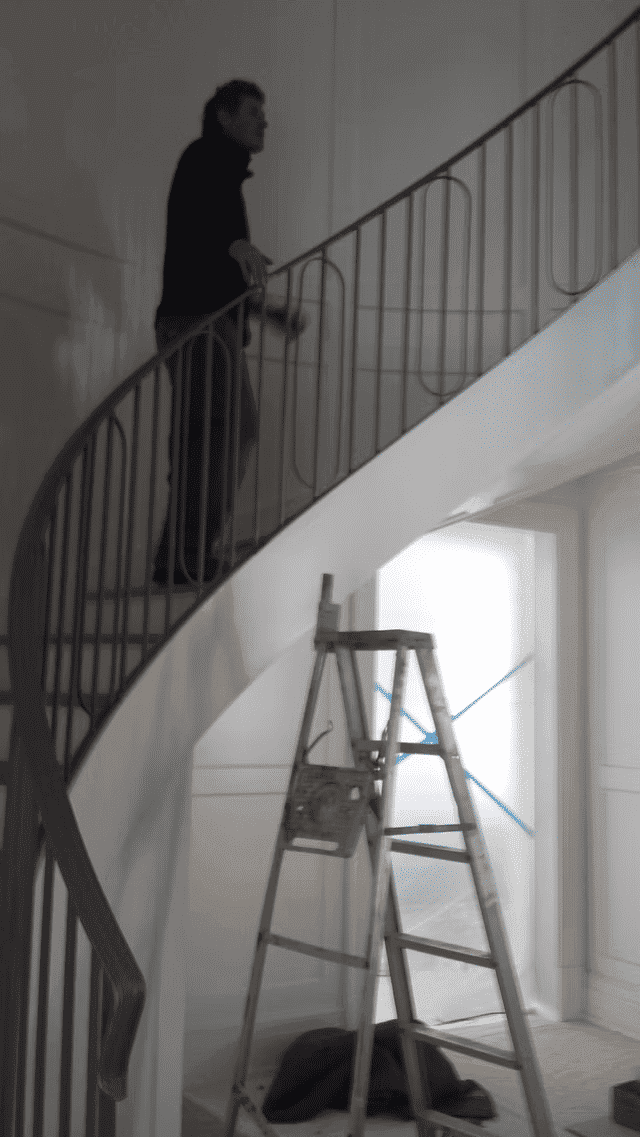 Person painting a staircase with a ladder, showcasing home improvement and interior design.