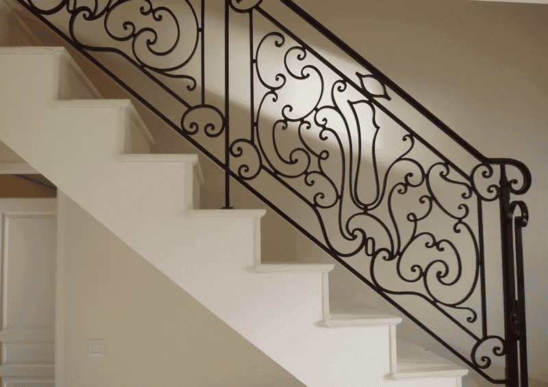 Elegant wrought iron staircase railing on white stairs in a modern interior setting.