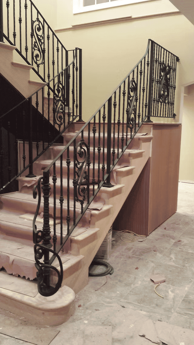 Elegant wooden staircase with ornate black iron railing in a home under renovation.