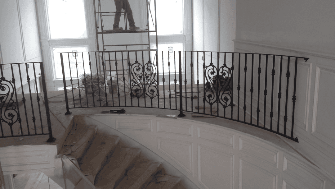 Elegant curved staircase railing with intricate black ironwork in a partially renovated interior.