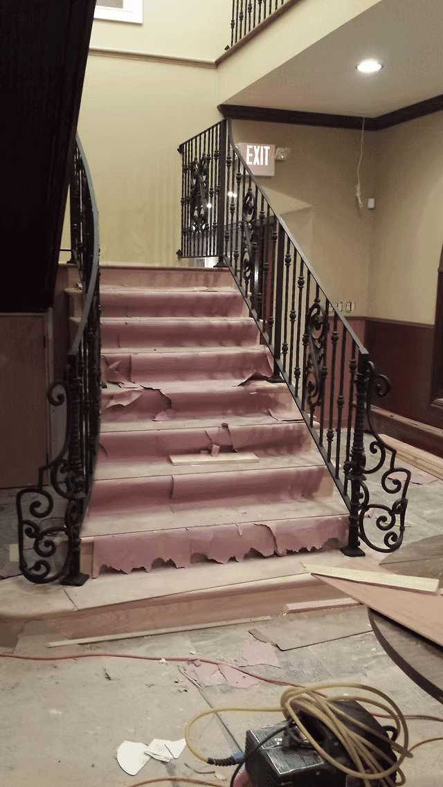 Staircase undergoing renovation with exposed steps and ornate metal railing.