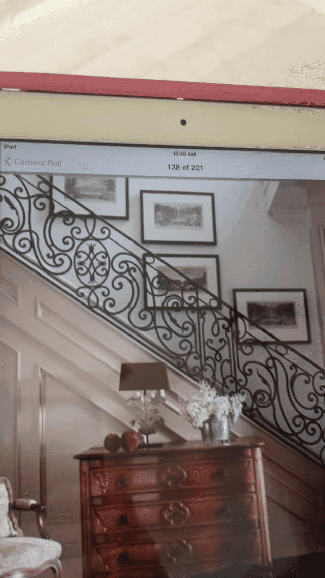 Elegant staircase with decorative iron railing, vintage frames, and a wooden chest of drawers.