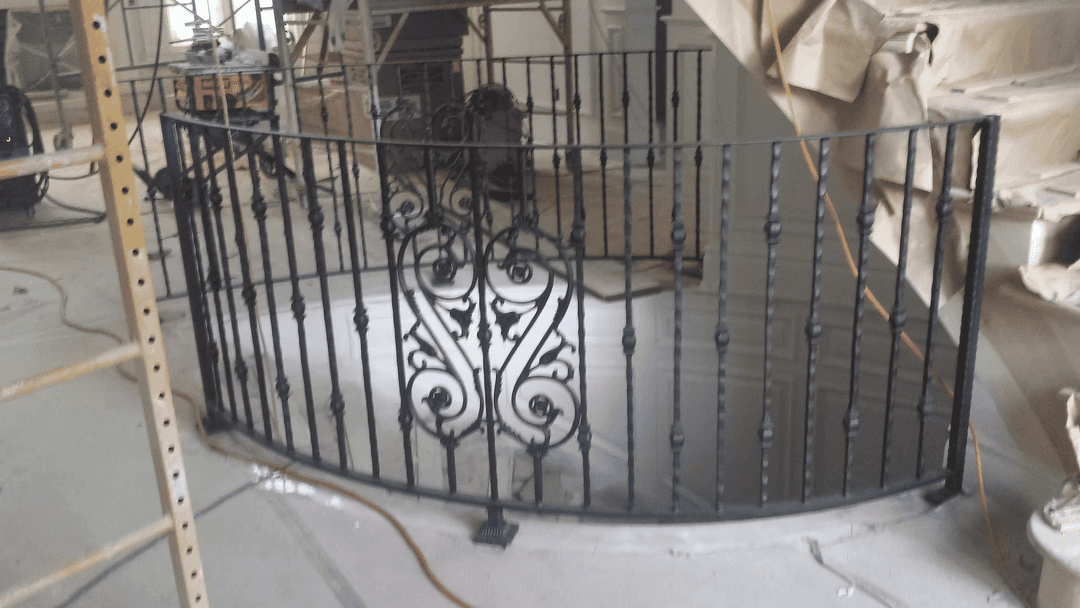 Wrought iron staircase railing with ornate design, under construction in a residential interior.