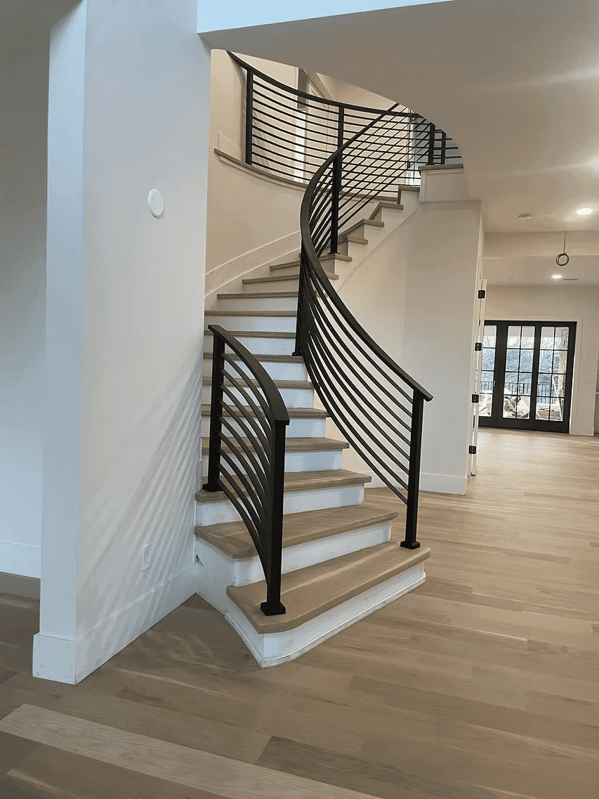 Curved staircase with black railing in modern home interior with hardwood floors.