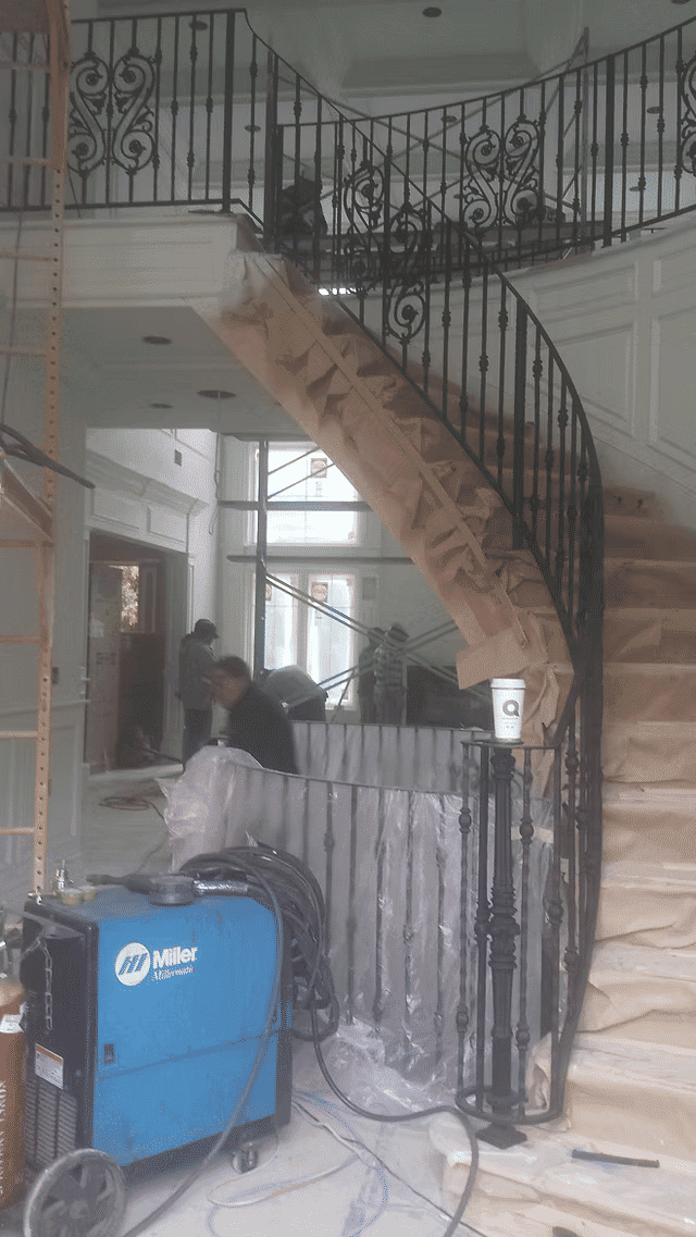 Elegant curved staircase under renovation in a well-lit modern home. Construction workers visible.
