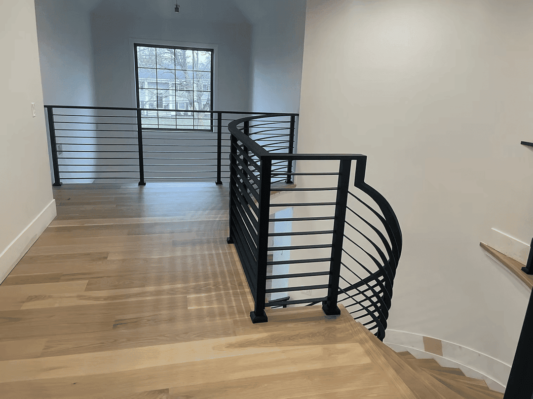 Modern stairwell featuring sleek black railings and natural wood flooring with ample natural light.
