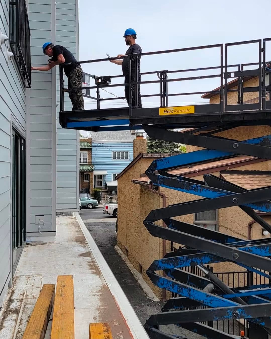 Workers using a lift to perform maintenance on a building exterior. Safety helmets are worn.