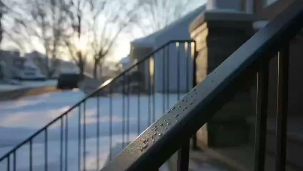 Metal handrail with water droplets, snowy landscape and morning light in the background.