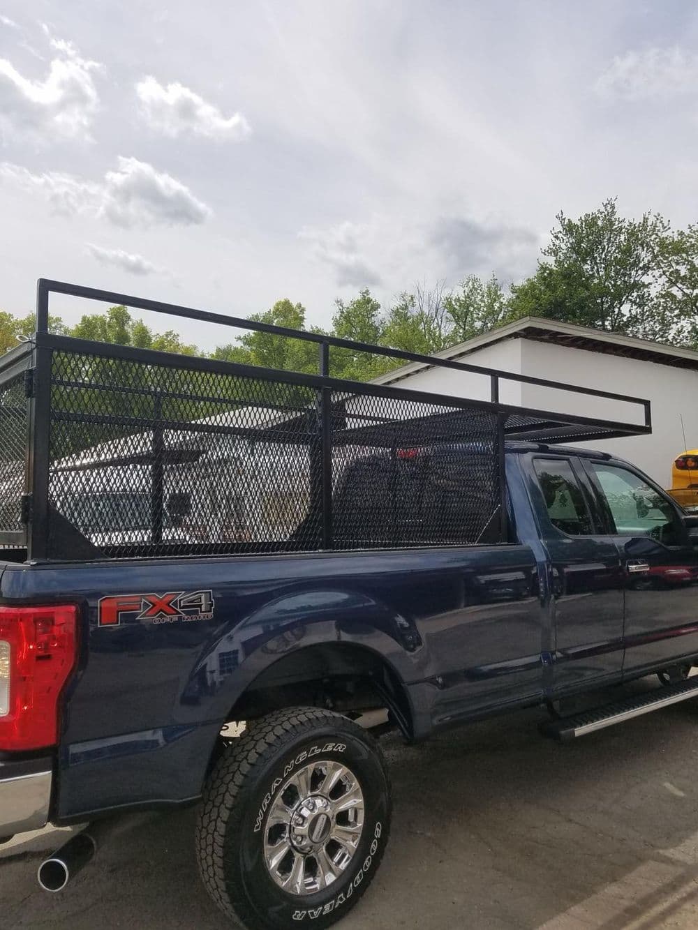 Blue pickup truck with metal rack, parked outdoors under a cloudy sky.