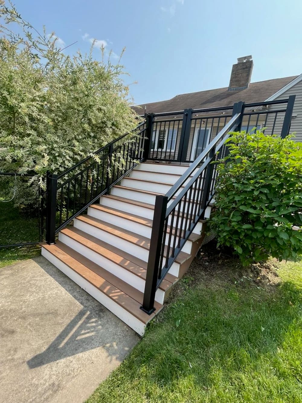 Stately outdoor staircase with modern black railings leading to a house, surrounded by greenery.
