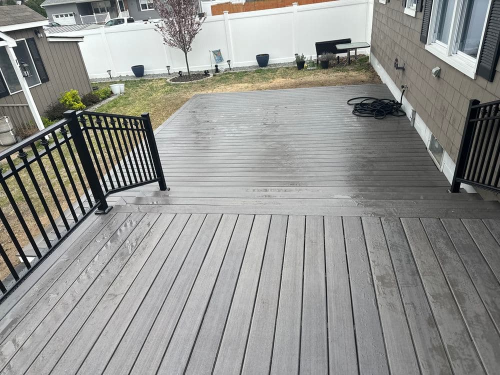 Newly built wooden deck with black railings, featuring wet surface after rain, in residential yard.