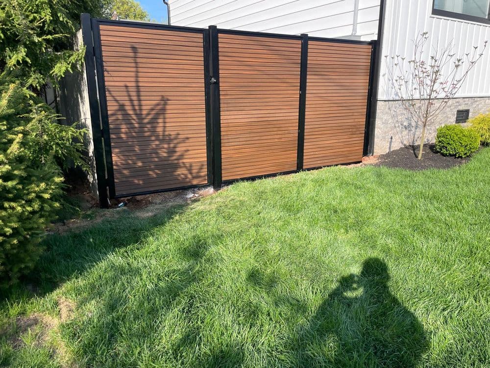 Modern horizontal wood fence with black metal framing in a green lawn setting.