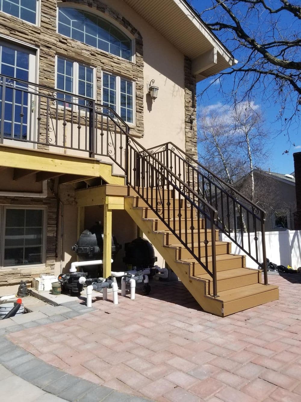 Wooden staircase with iron railing leading to a modern home, surrounded by landscaped patio.